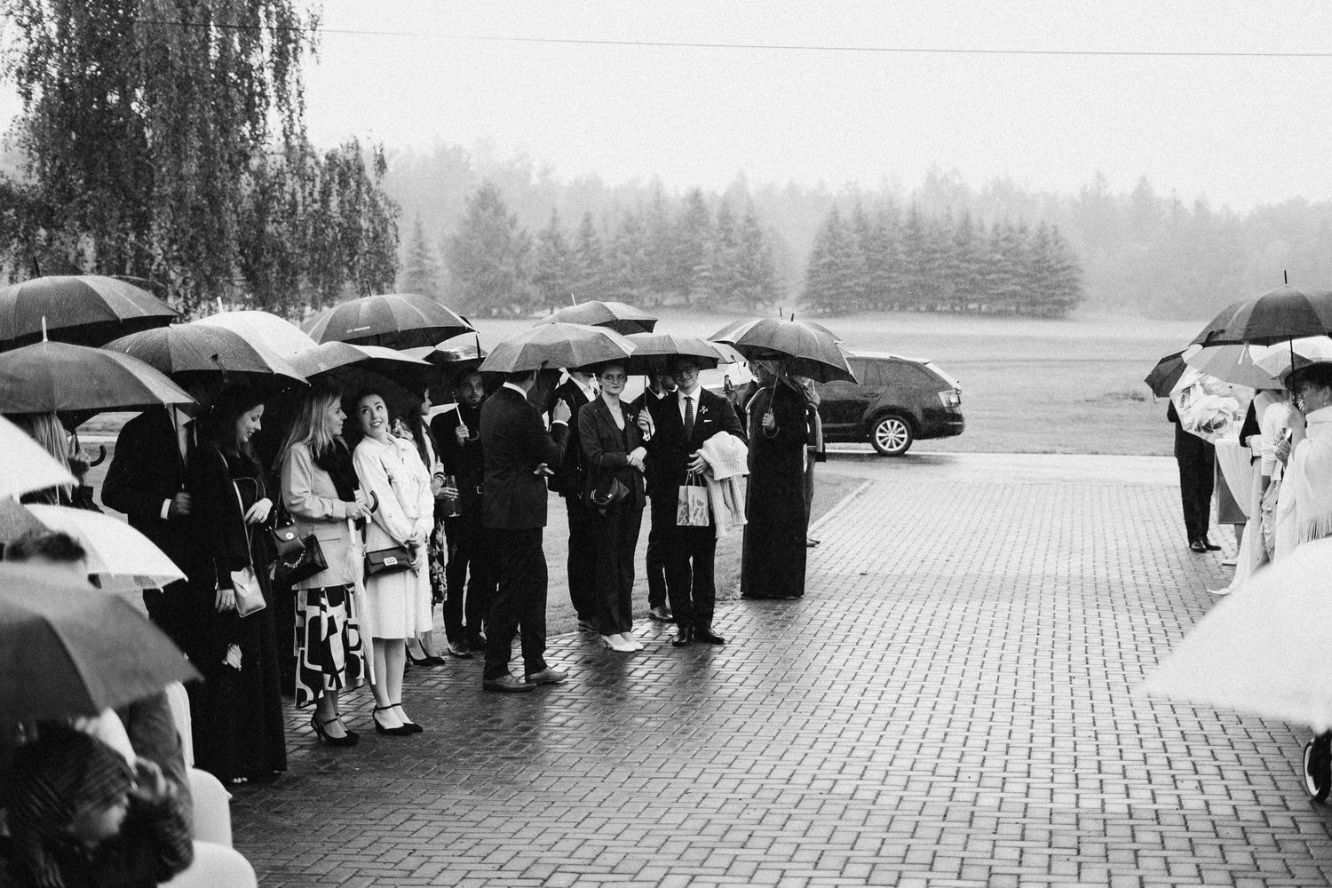 A rainy day somber gathering with umbrellas outside what appears to be a military memorial service in black and white.