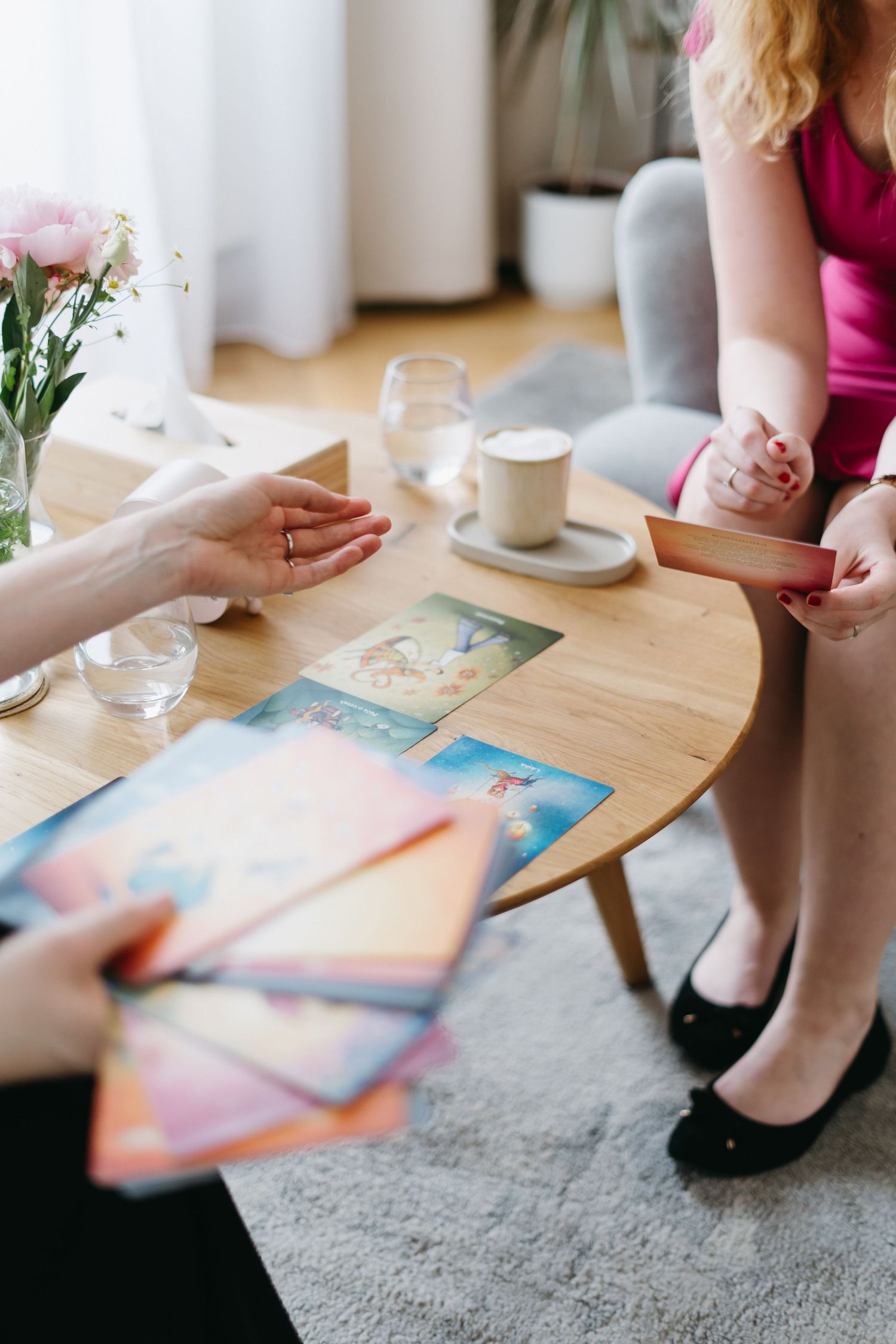 Two people having coffee at wooden table while looking at colorful photographs with flowers in vase nearby.