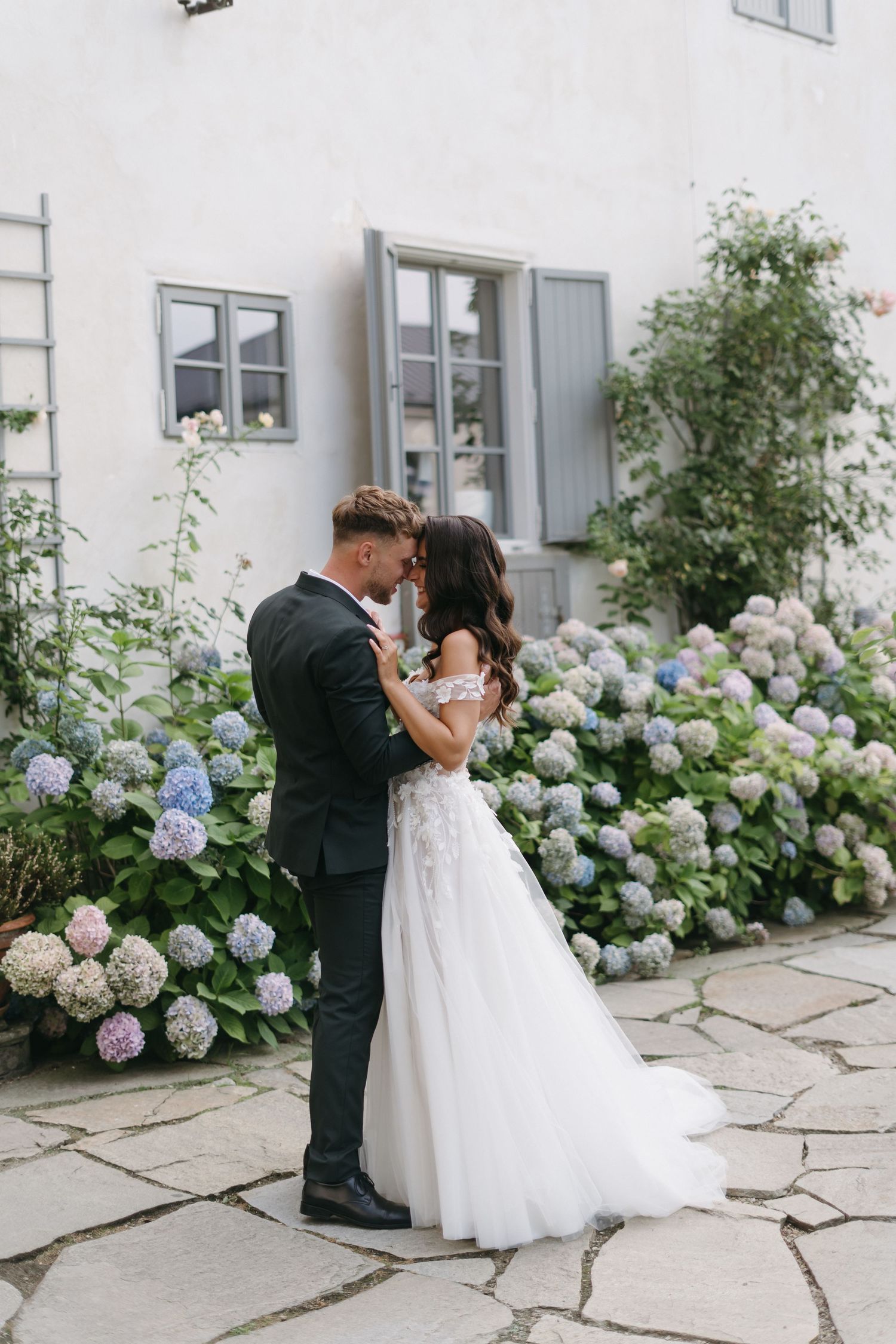 A romantic wedding scene against a wall of blooming hydrangeas with a couple embracing in a series of shots.