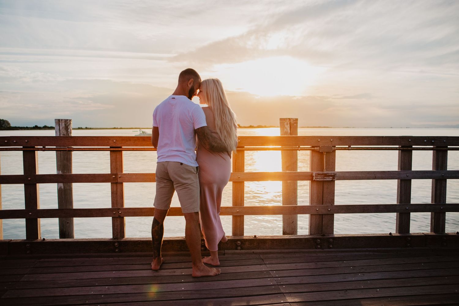 Couple sharing romantic moment on wooden pier during sunset.