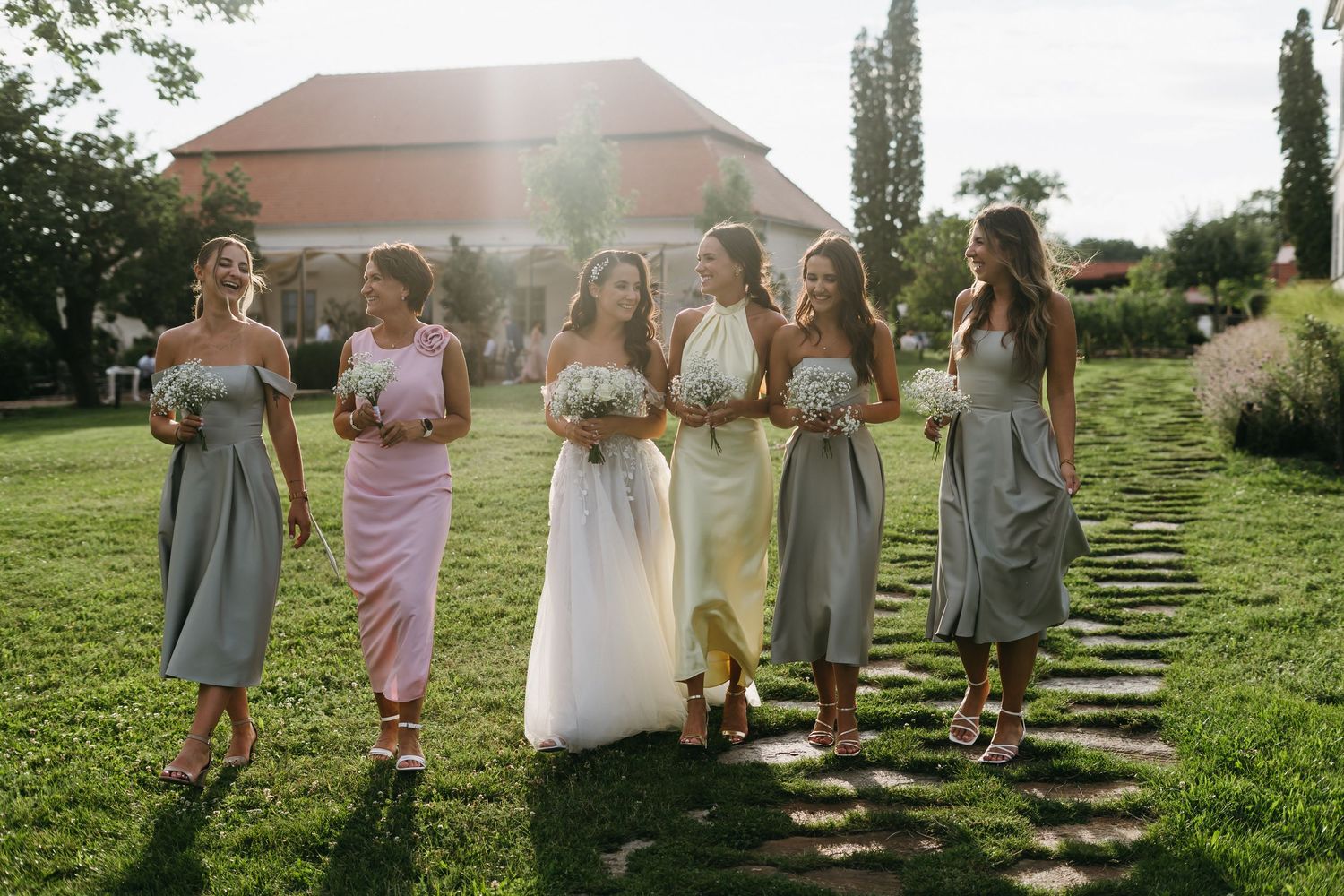 Wedding party walks through a garden pathway in afternoon sunlight, creating joyful candid moments.