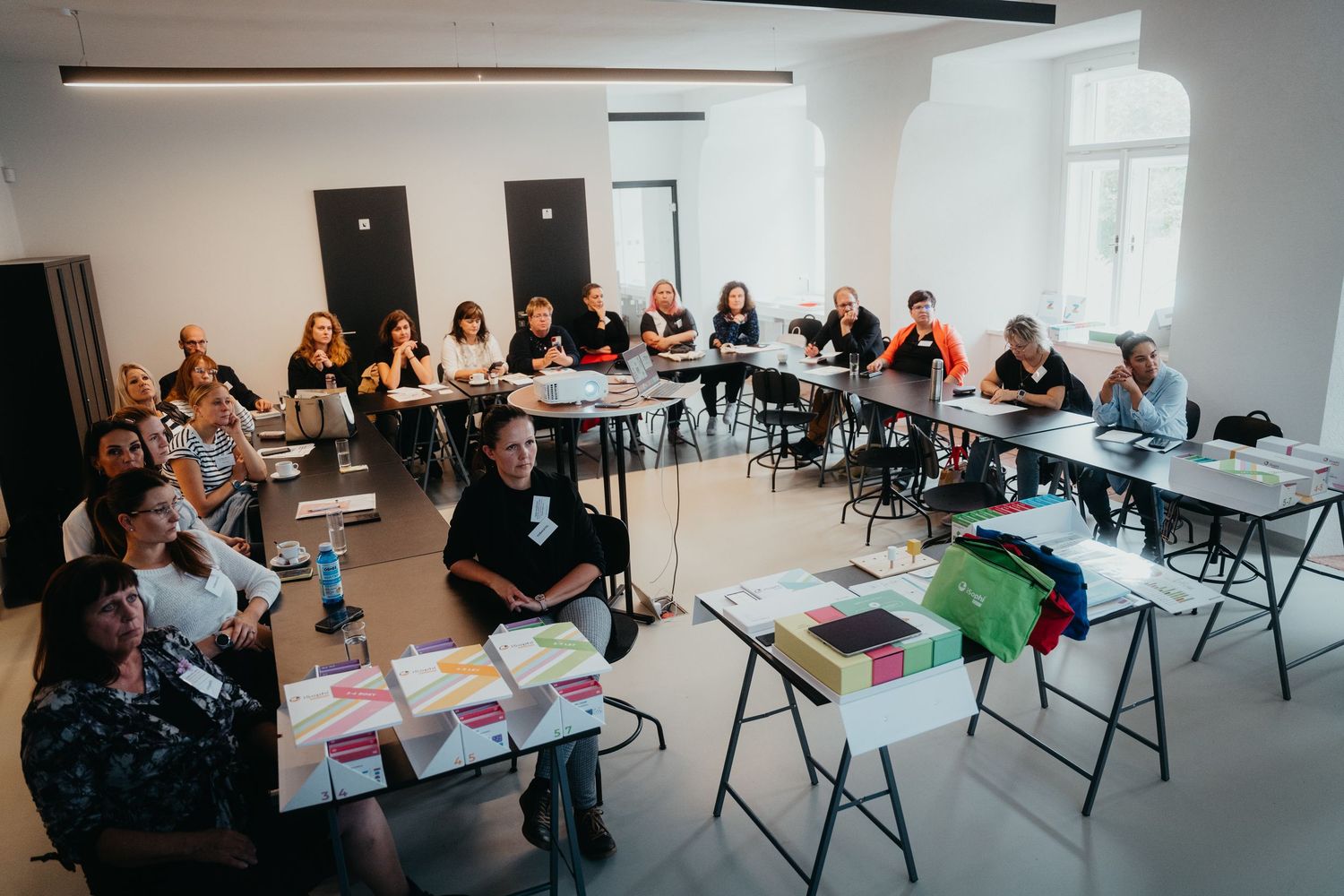 Panoramic view of workshop participants seated at long tables in a bright meeting space.