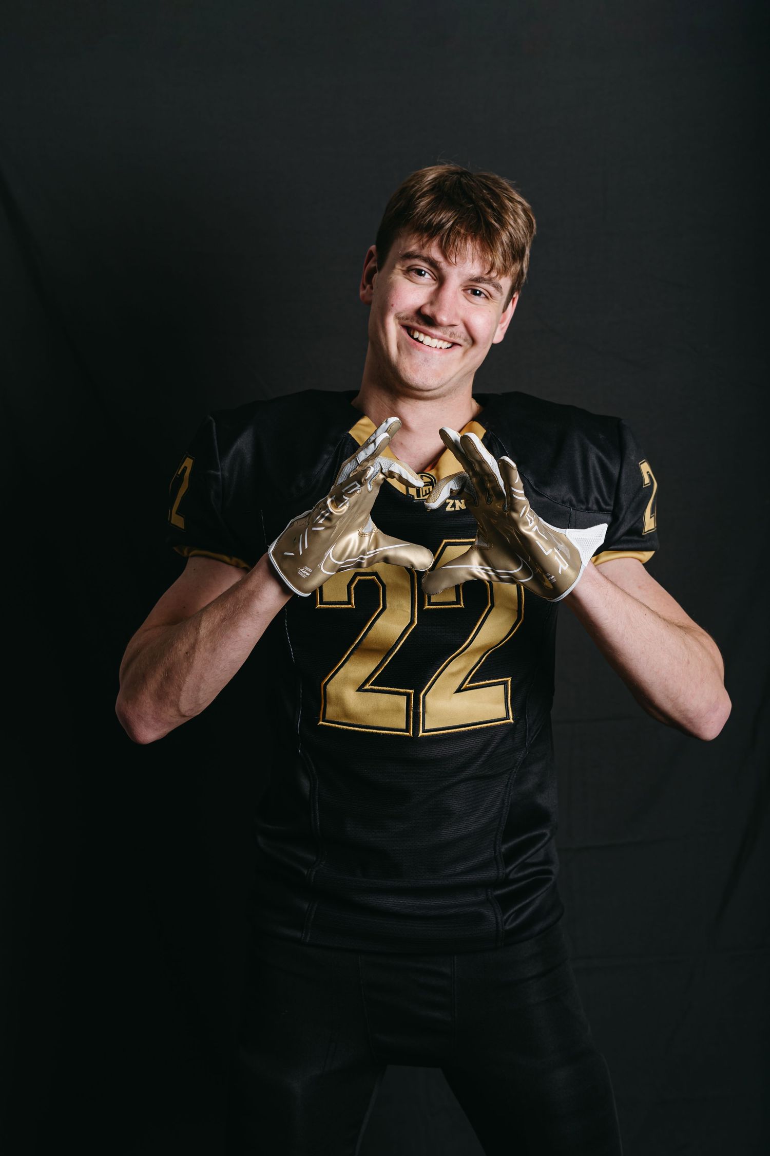 Football player in black jersey with number 22 makes heart shape gesture against dark background.