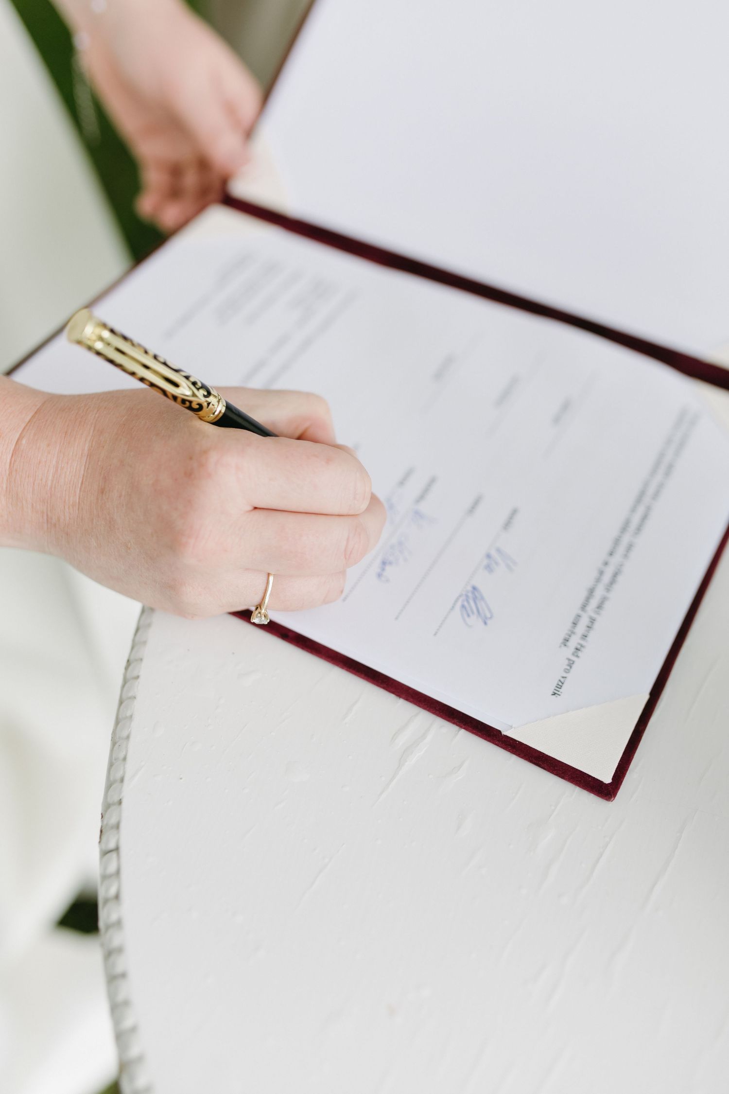 Close-up view of hands signing official documents on white paper with red binding.