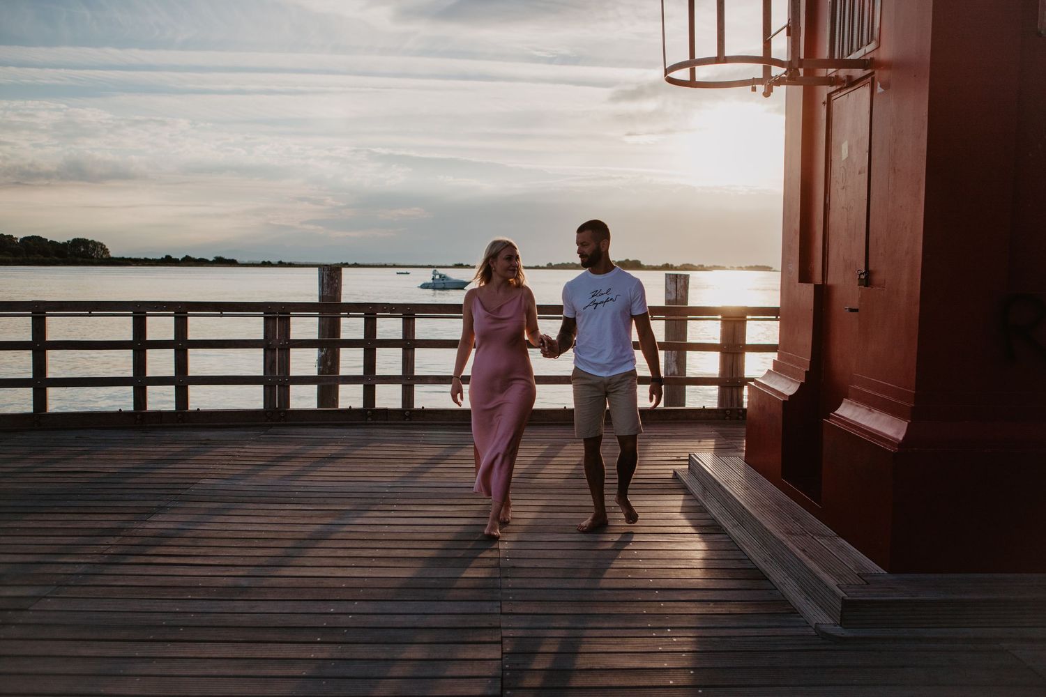 Couple walking hand in hand on wooden pier during sunset.