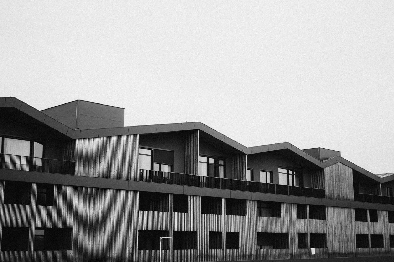 Modern apartment complex with angular architecture features vertical wood paneling and multiple levels in black and white.