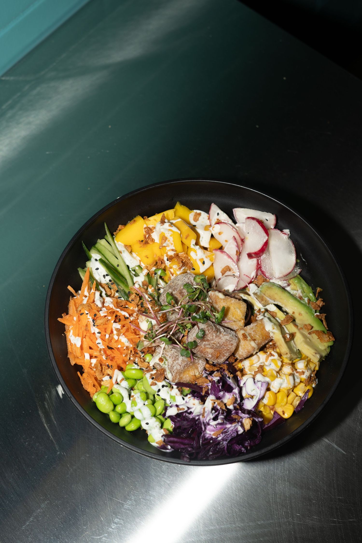 A black plate showcasing a colorful salad with fresh vegetables, meat, and vibrant toppings arranged in neat rows.