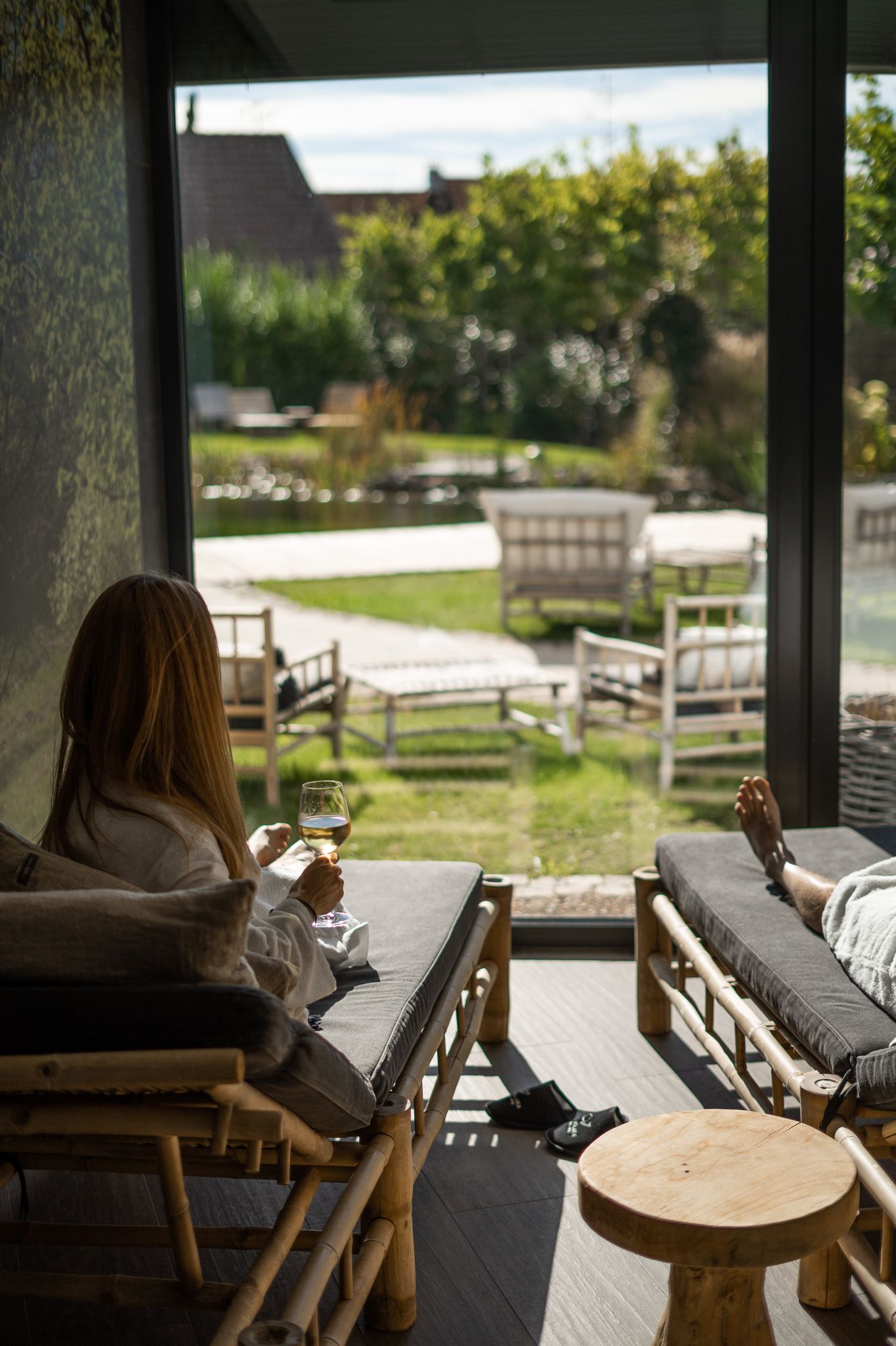 Person relaxing with a drink on an outdoor covered porch with rustic wooden furniture and scenic views.