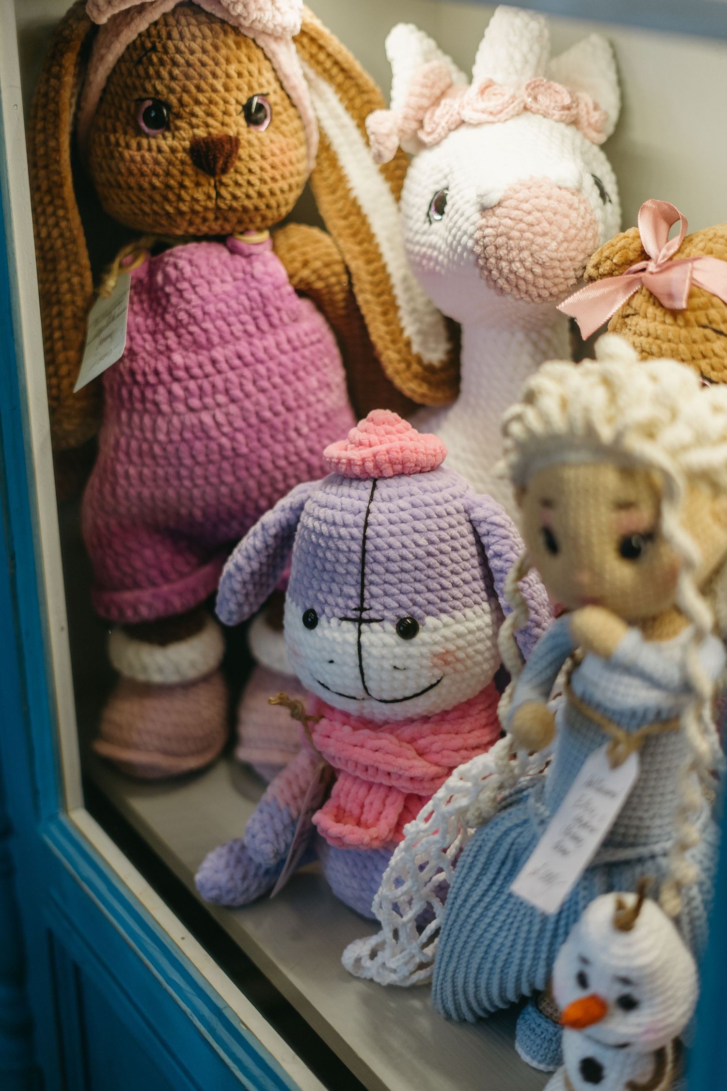 Collection of handmade knitted or crocheted stuffed animal toys on display including bunnies and bears in soft pastel colors.