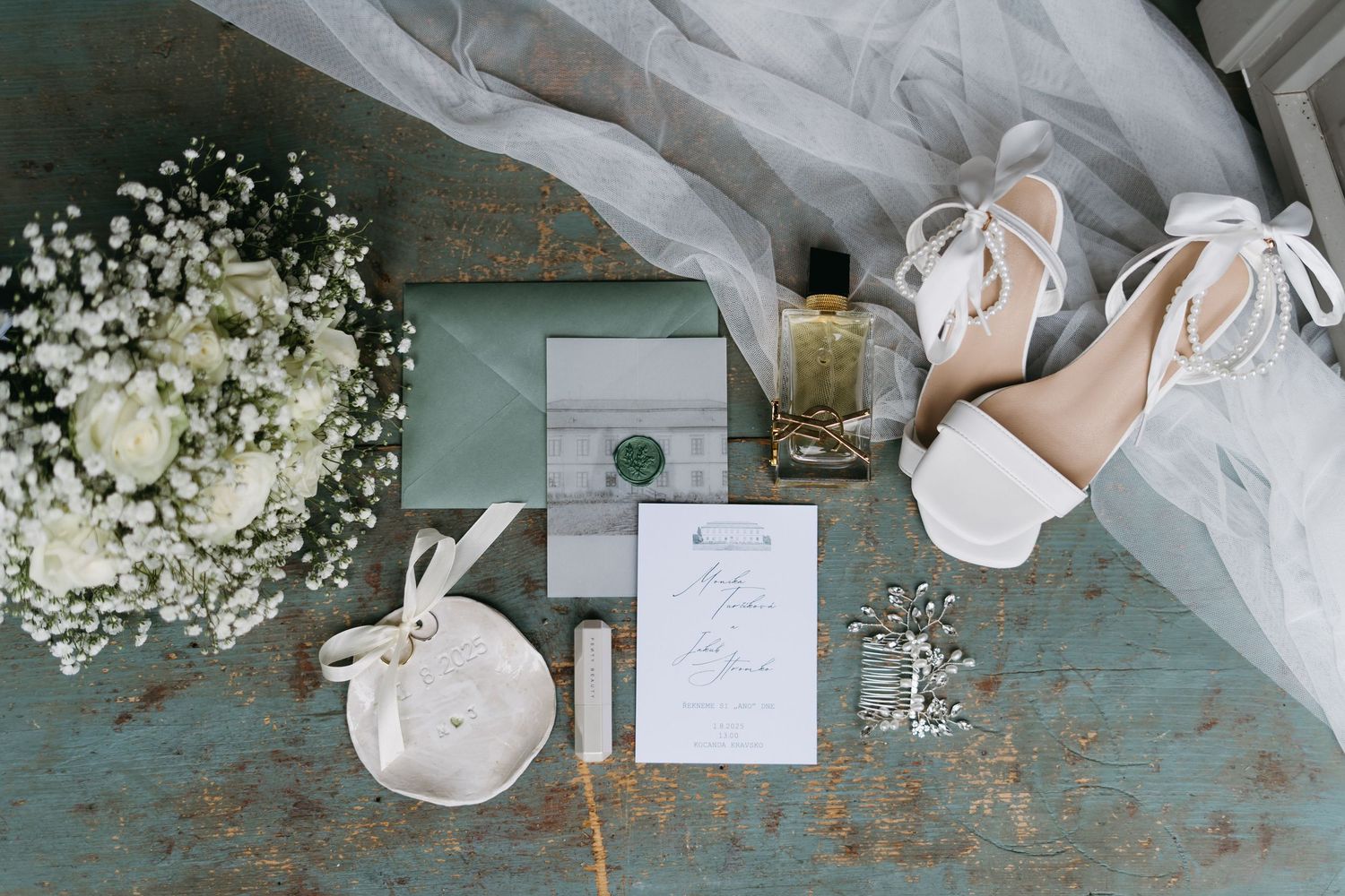 Elegant white wedding details including invitations, baby's breath flowers, and delicate ribbons on a rustic turquoise surface.