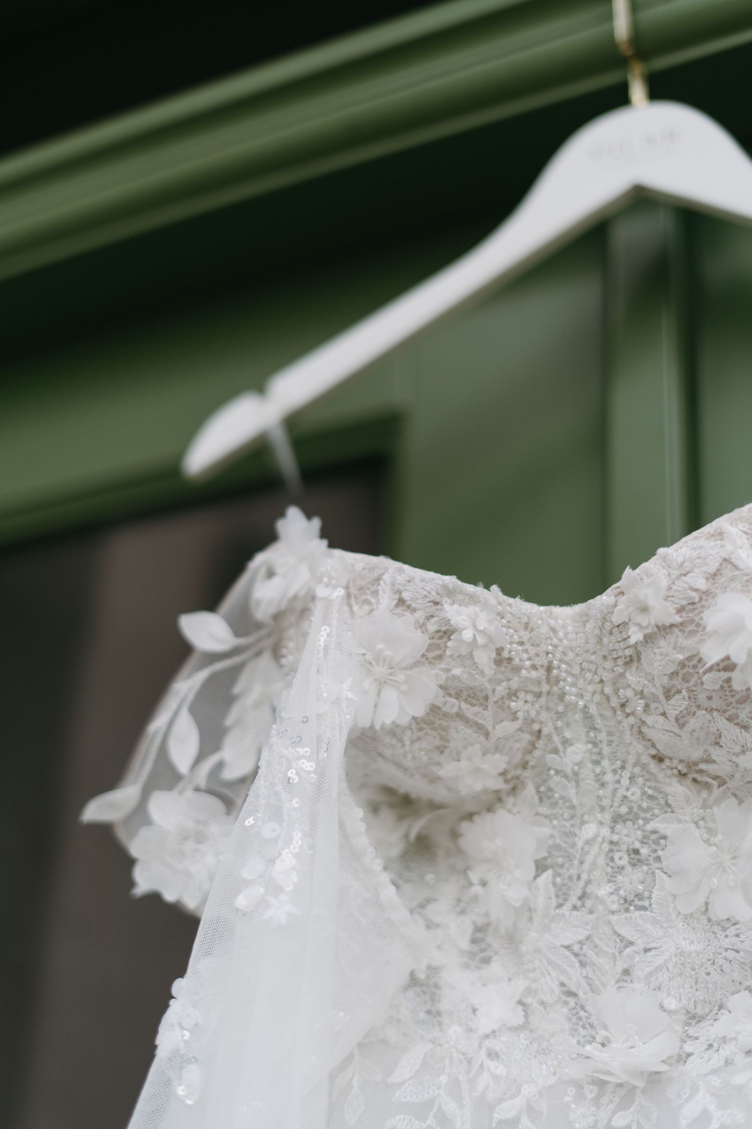 Close-up detail of delicate lace and beading on a white wedding dress hanging on white hanger.