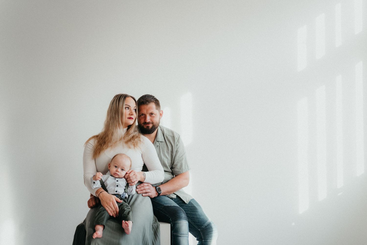Family sitting together in bright minimal setting against white wall with sunlight.