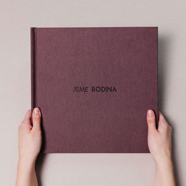 Hands holding and opening a burgundy-colored photo album or book against a light gray background.