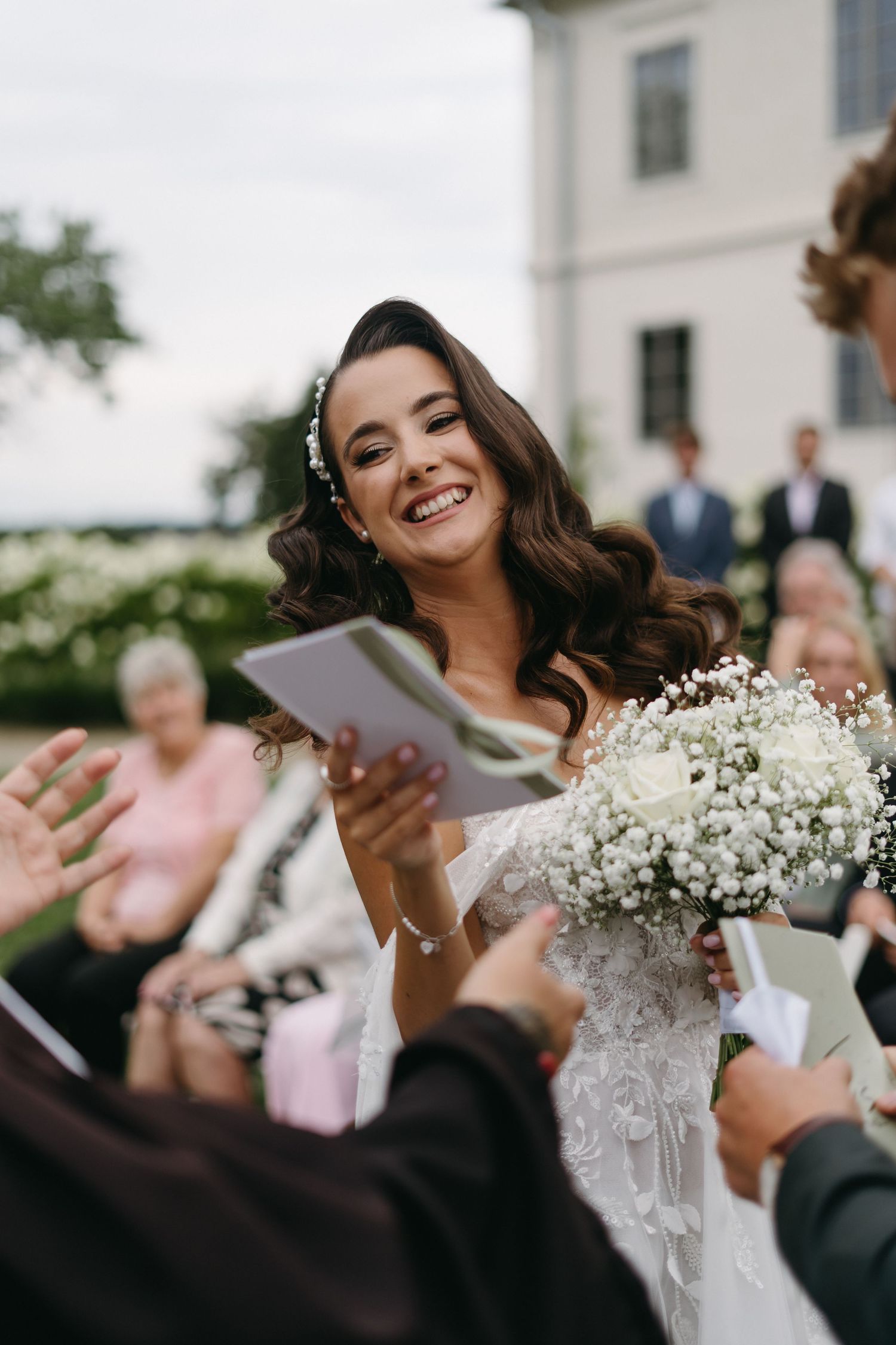 A joyful moment at a wedding with baby's breath bouquet, white dress and veil against a white building.