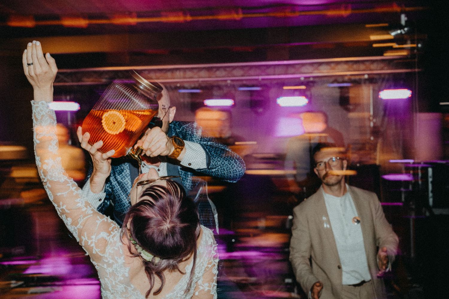 Blurred motion shot of people dancing at a nightclub with purple lighting and neon effects in background.