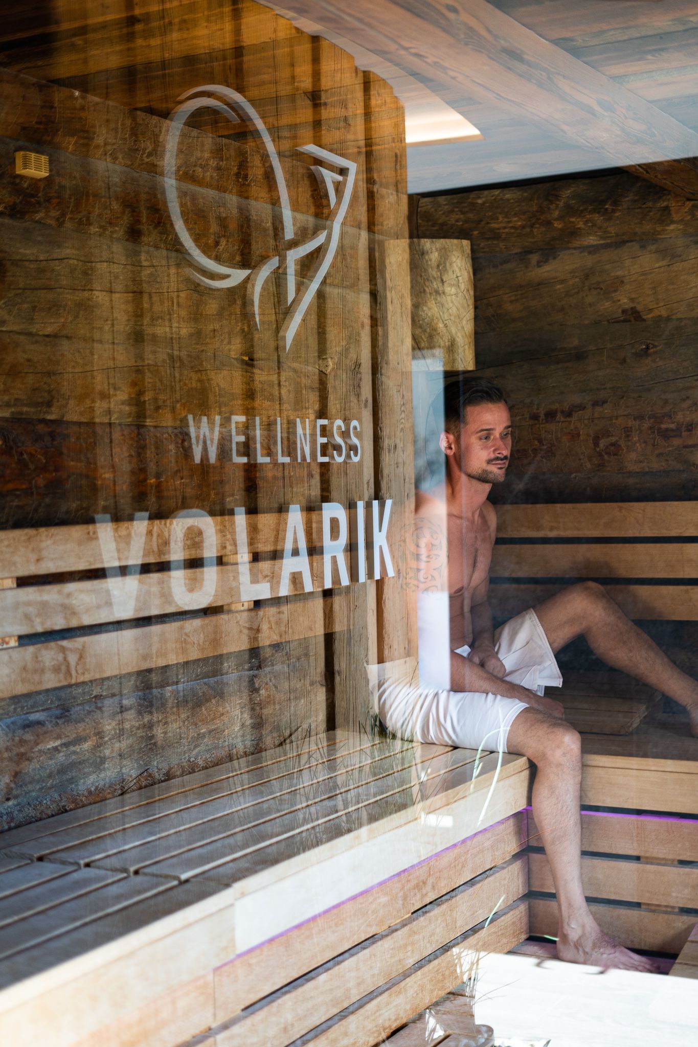 Wooden sauna interior with bench seating showing wellness logo and natural lighting.