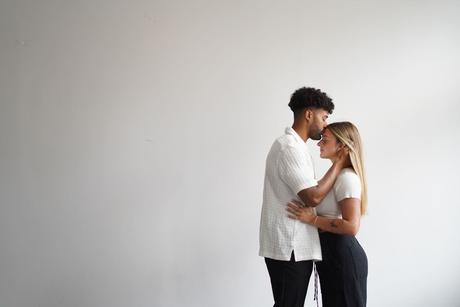 Intimate portrait of couple embracing against minimalist white wall background.