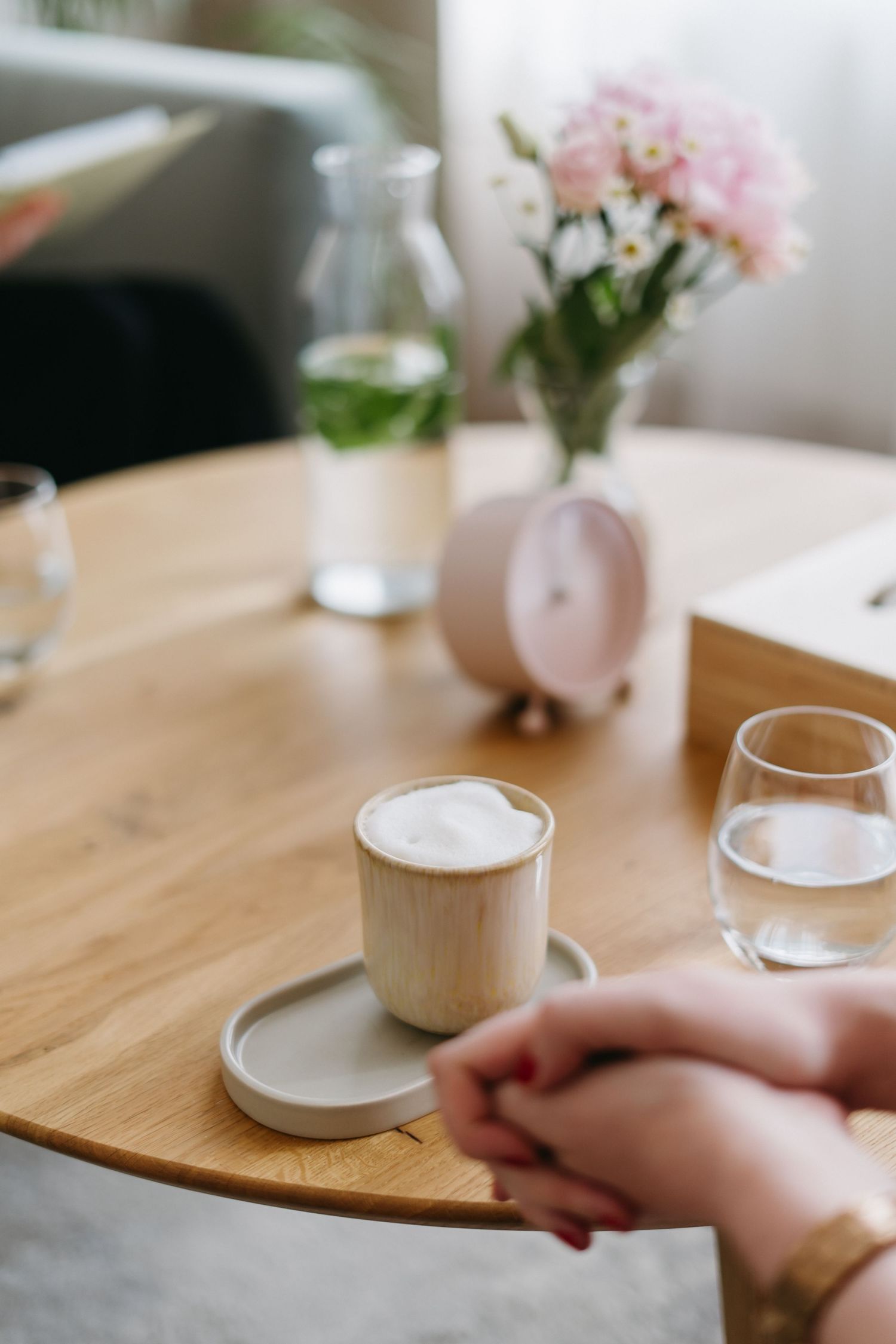 Close up of coffee and pink flowers on wooden table with hands clasped during casual meeting.
