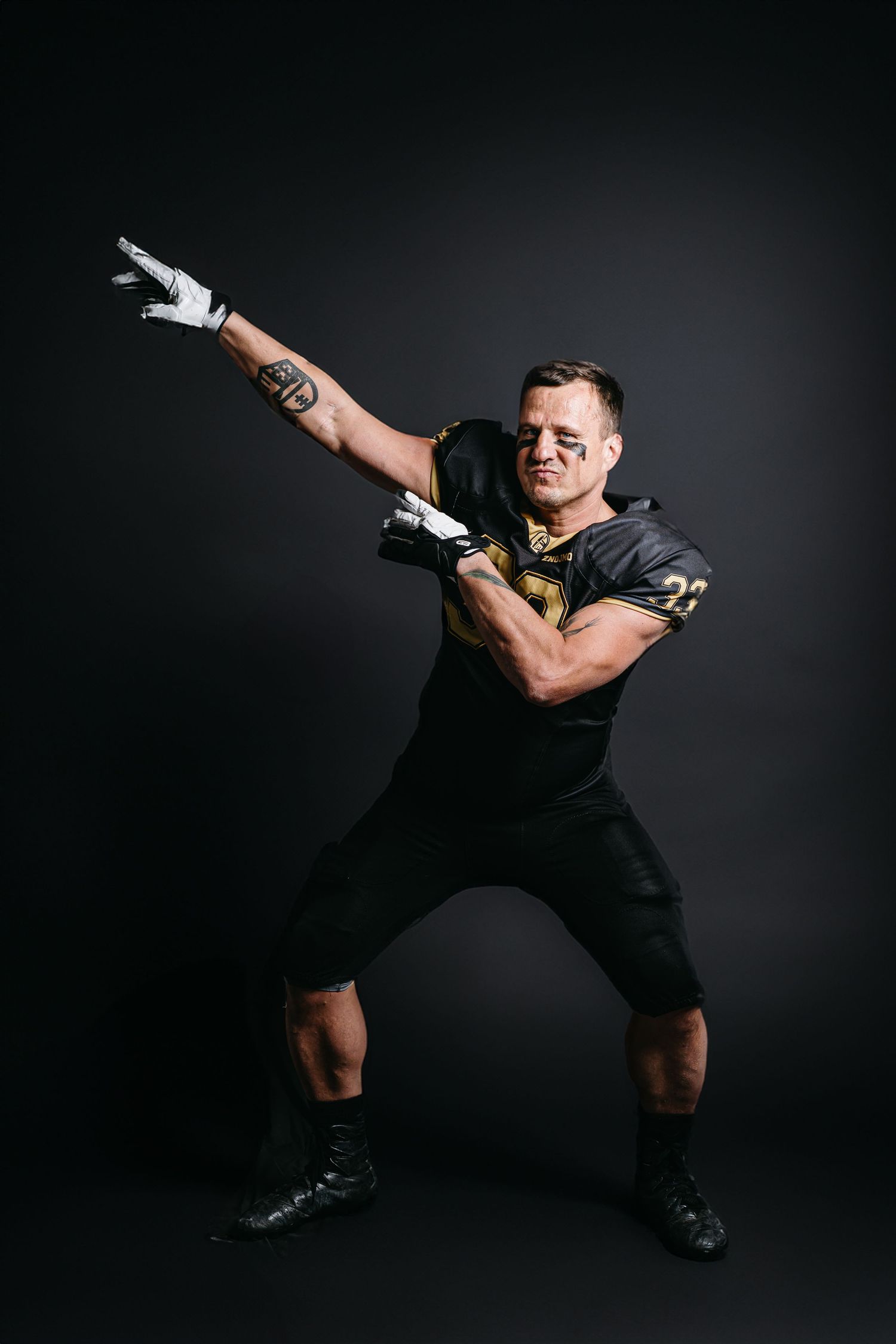 Athletic figure in black athletic wear strikes dynamic pose against dark background while wearing gloves.