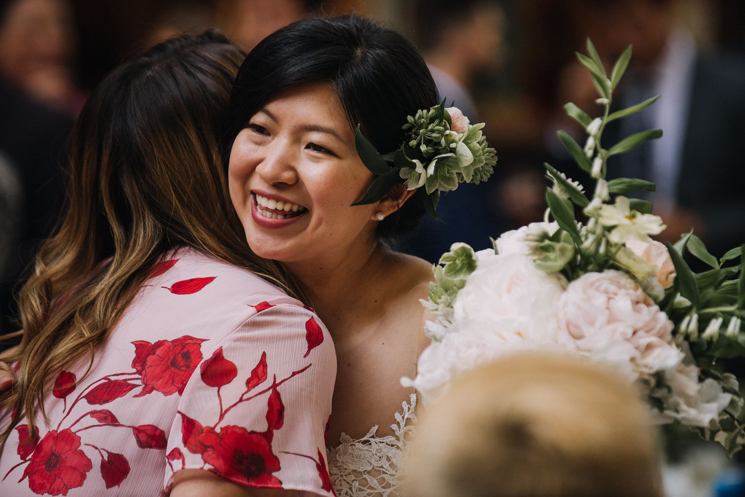 Wedding guests laugh and smile during an outdoor celebration surrounded by floral decorations and greenery.