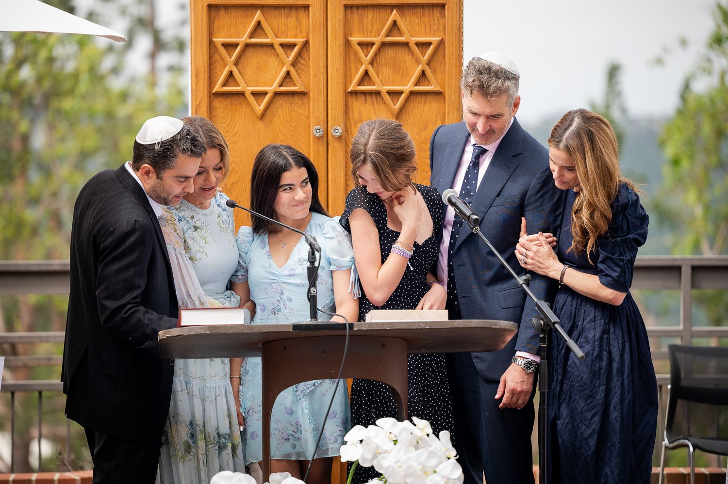 A group gathers at an outdoor ceremony signing documents at a wooden table with Star of David symbols visible.