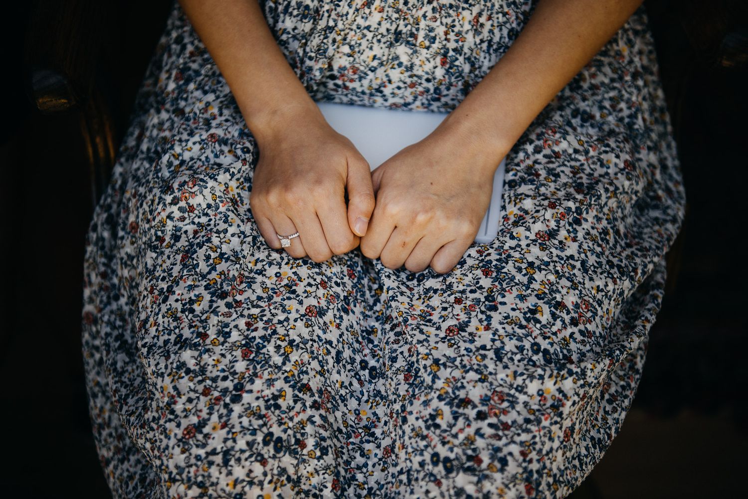 Close-up view of hands resting on a floral print dress against a dark background.