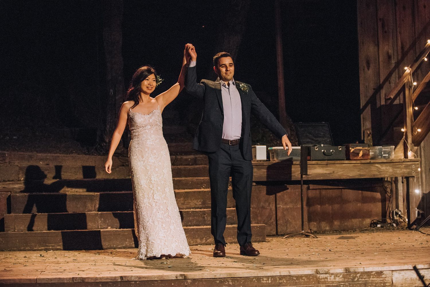 A couple shares their first dance as newlyweds on a rustic wooden stage at an outdoor wedding reception.