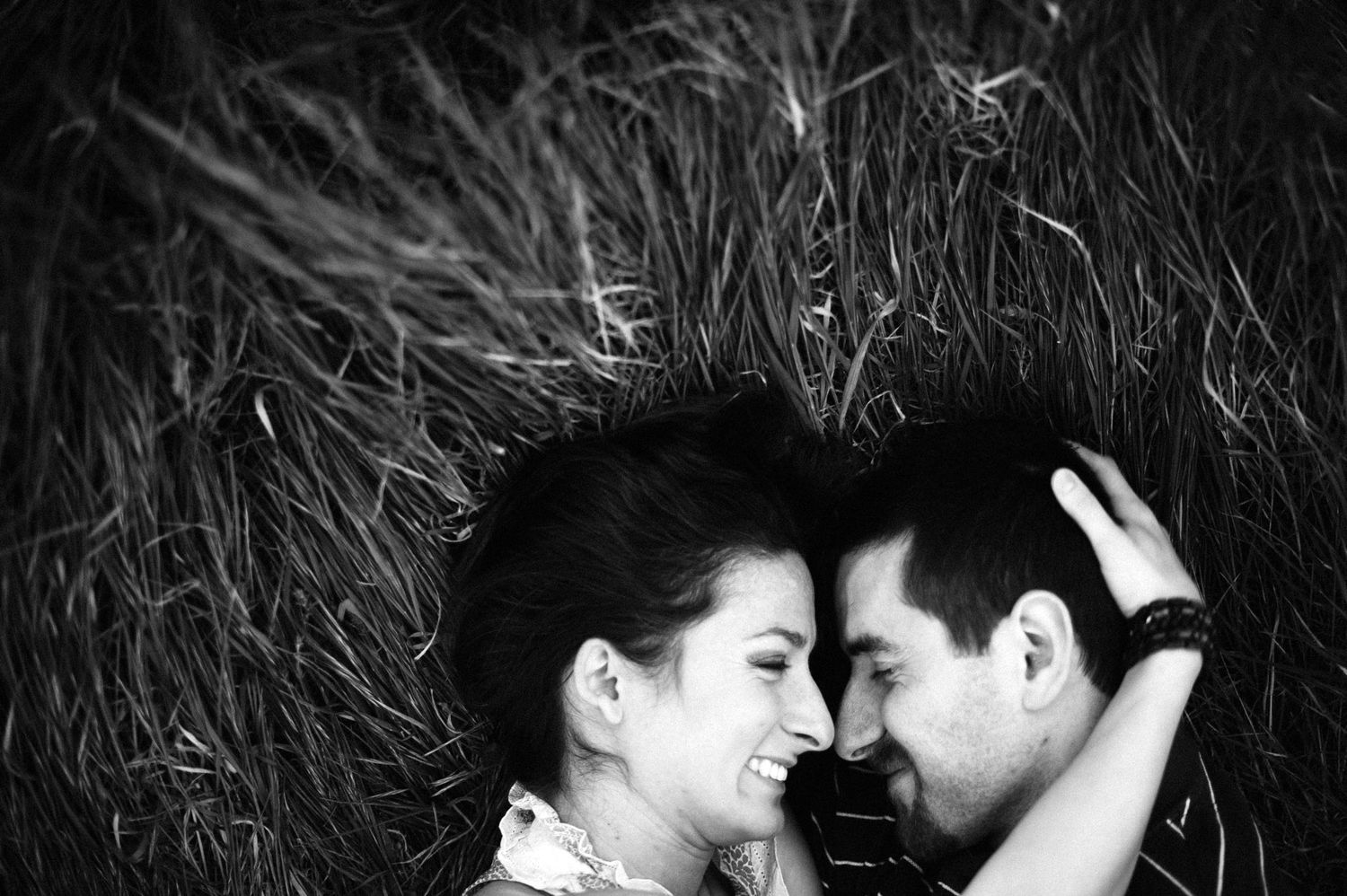 A romantic black and white photograph of a couple lying in tall grass with their faces close together.
