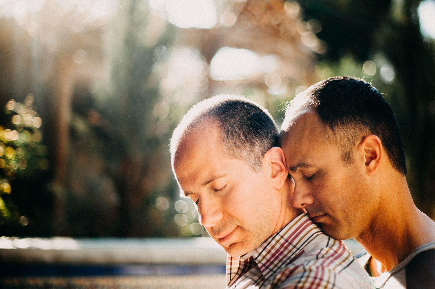 Two people share an intimate moment in dappled sunlight outdoors.