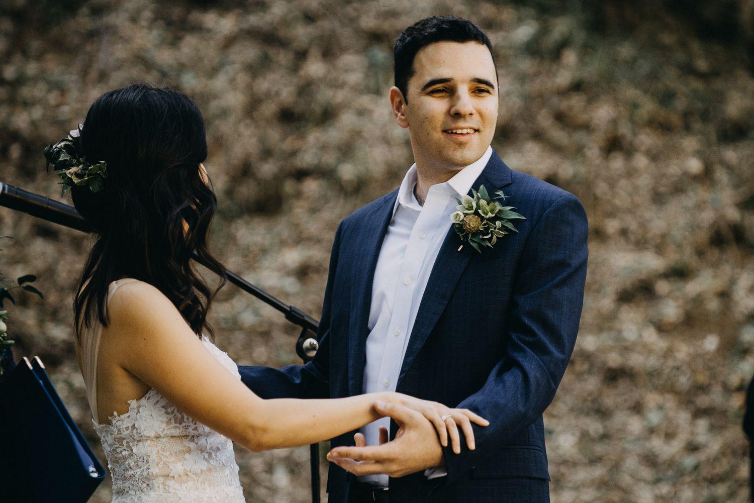 A couple shares an intimate moment during their wedding ceremony in an outdoor woodland setting.