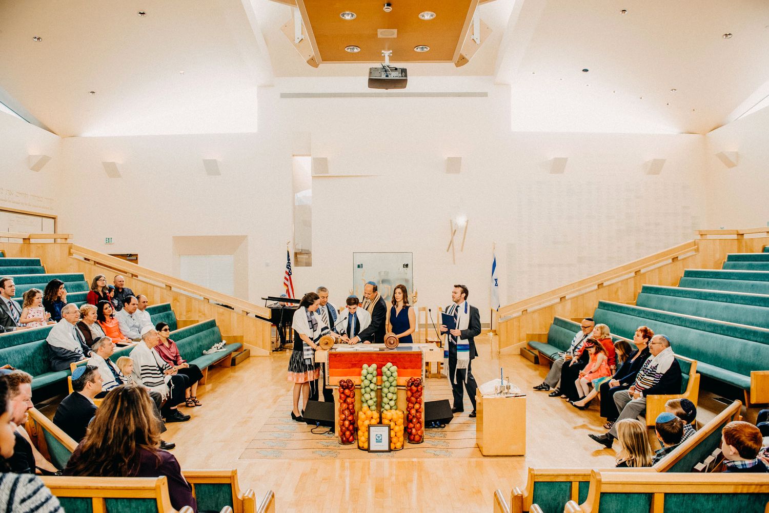 An indoor wedding ceremony in a bright chapel with wooden pews and people gathered around a decorated altar.