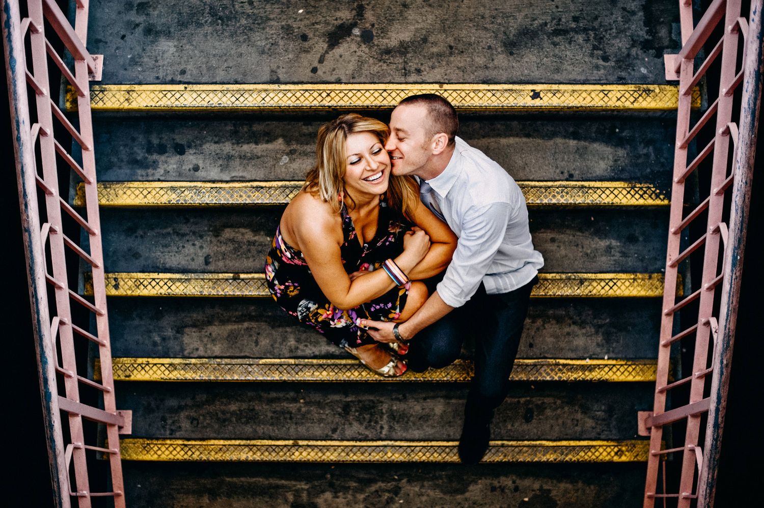 A couple sits intimately together on yellow striped steps during an outdoor photoshoot.
