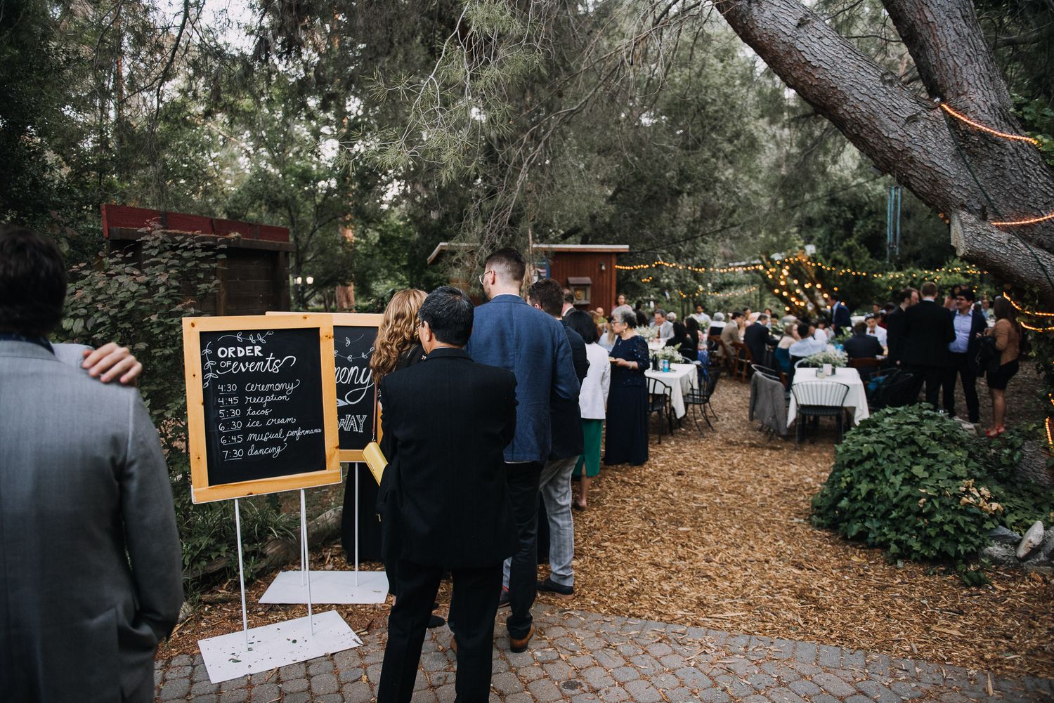 Outdoor wedding venue decorated with rustic wooden signs and autumn leaves scattered along a garden pathway.
