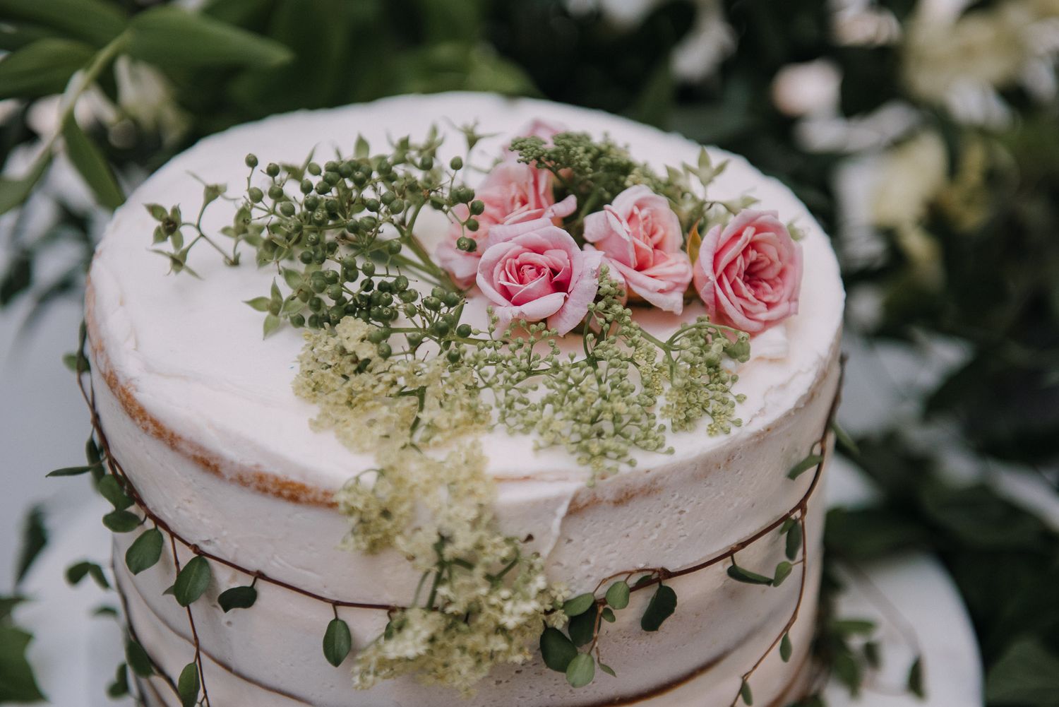 A rustic white wedding cake decorated with delicate pink roses and baby's breath on a wooden stand.