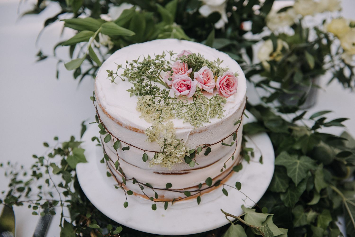 Wedding cake decorated with fresh flowers and greenery displayed on white plates with delicate details.
