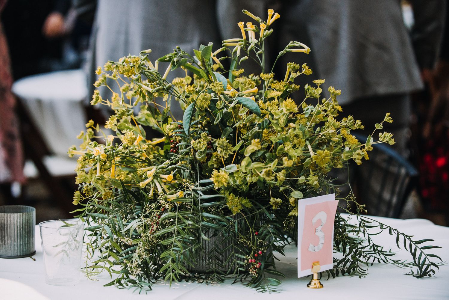 Yellow and green floral arrangements on a white tablecloth create an elegant wedding reception centerpiece display.