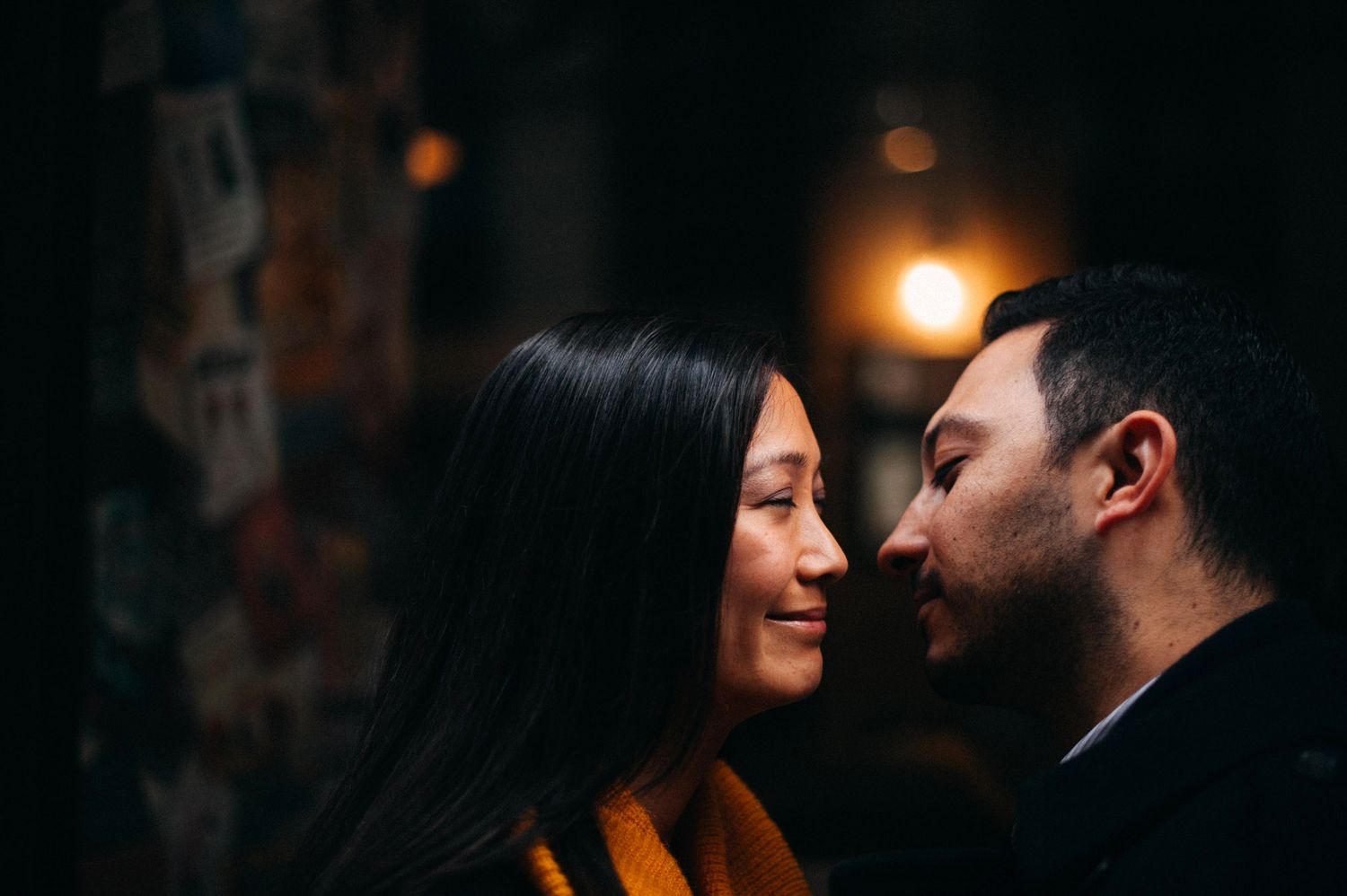 A couple in a romantic moment share an intimate pose against a dark moody background with glowing lights.