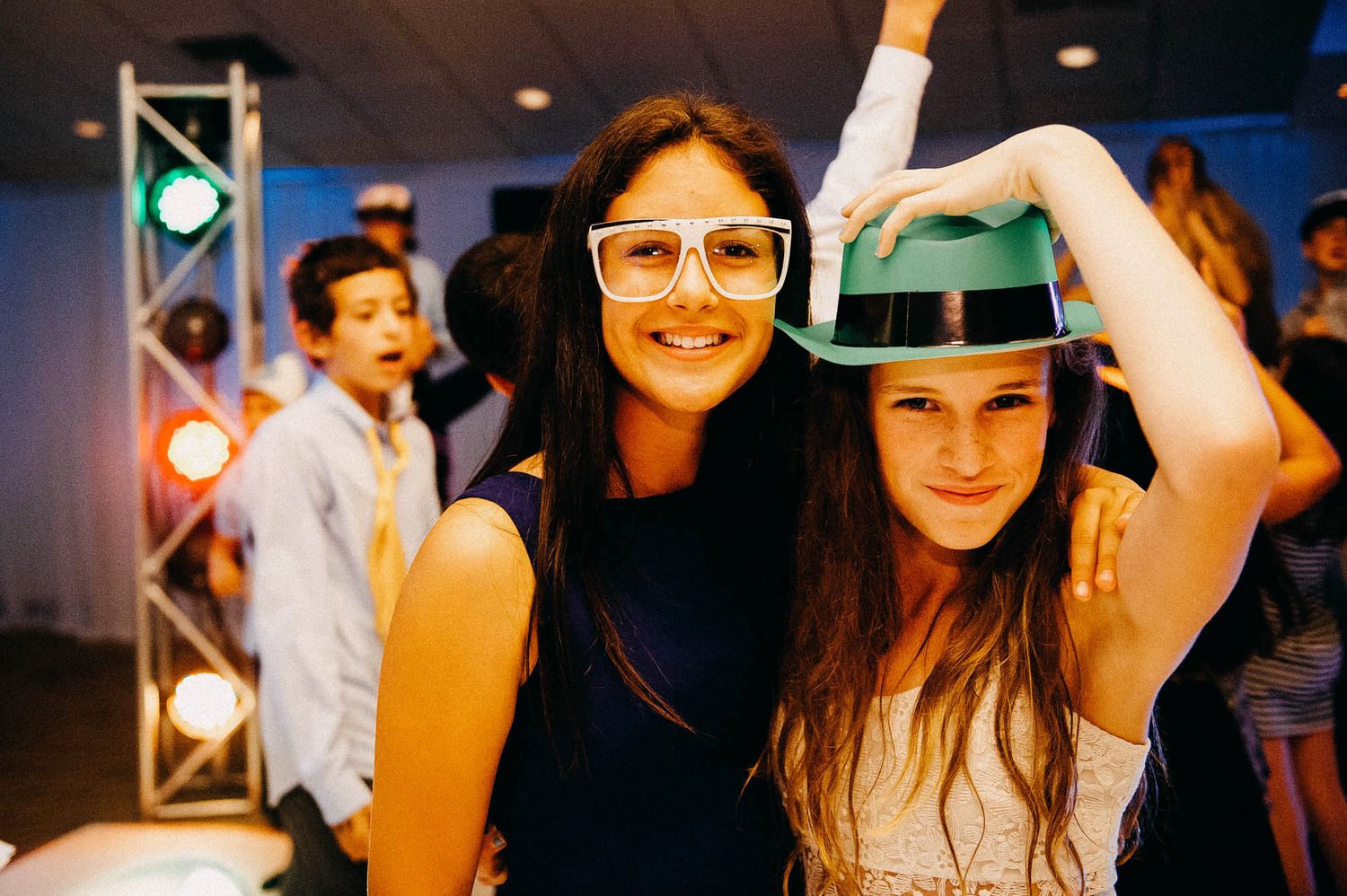 Two party guests enjoying themselves at a nightclub with one wearing glasses and another in a baseball cap.