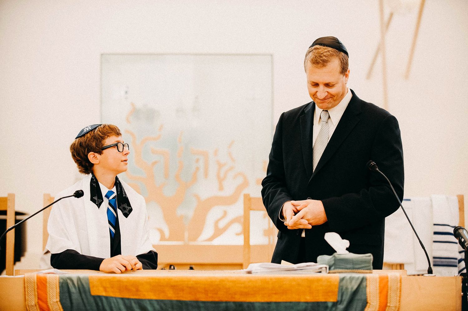 Two people in formal attire sit at a table with microphones during what appears to be an official meeting or event.