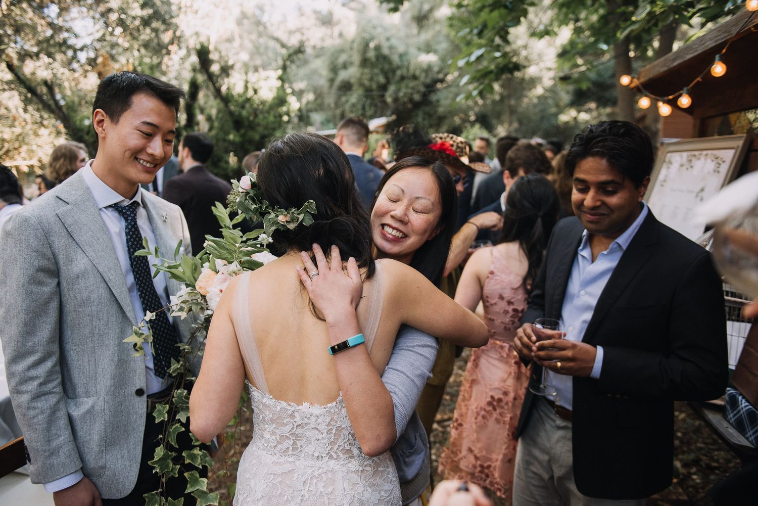 Wedding guests mingle and celebrate at an outdoor reception with string lights and natural decor.