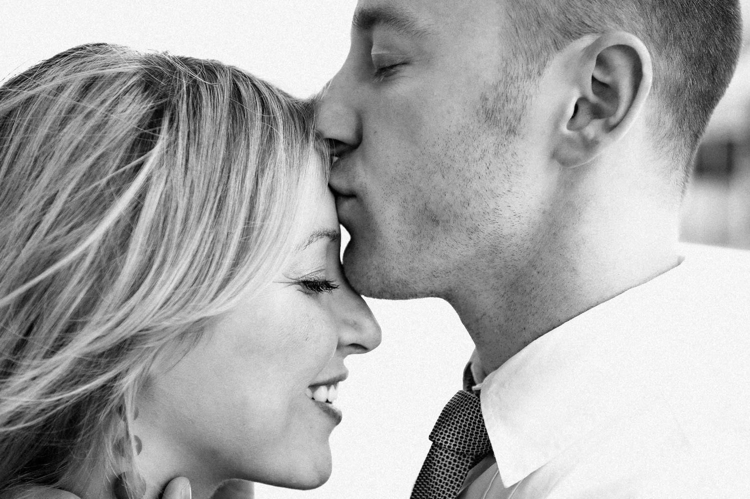 Black and white close-up of an intimate romantic moment between a couple smiling and sharing a tender kiss.