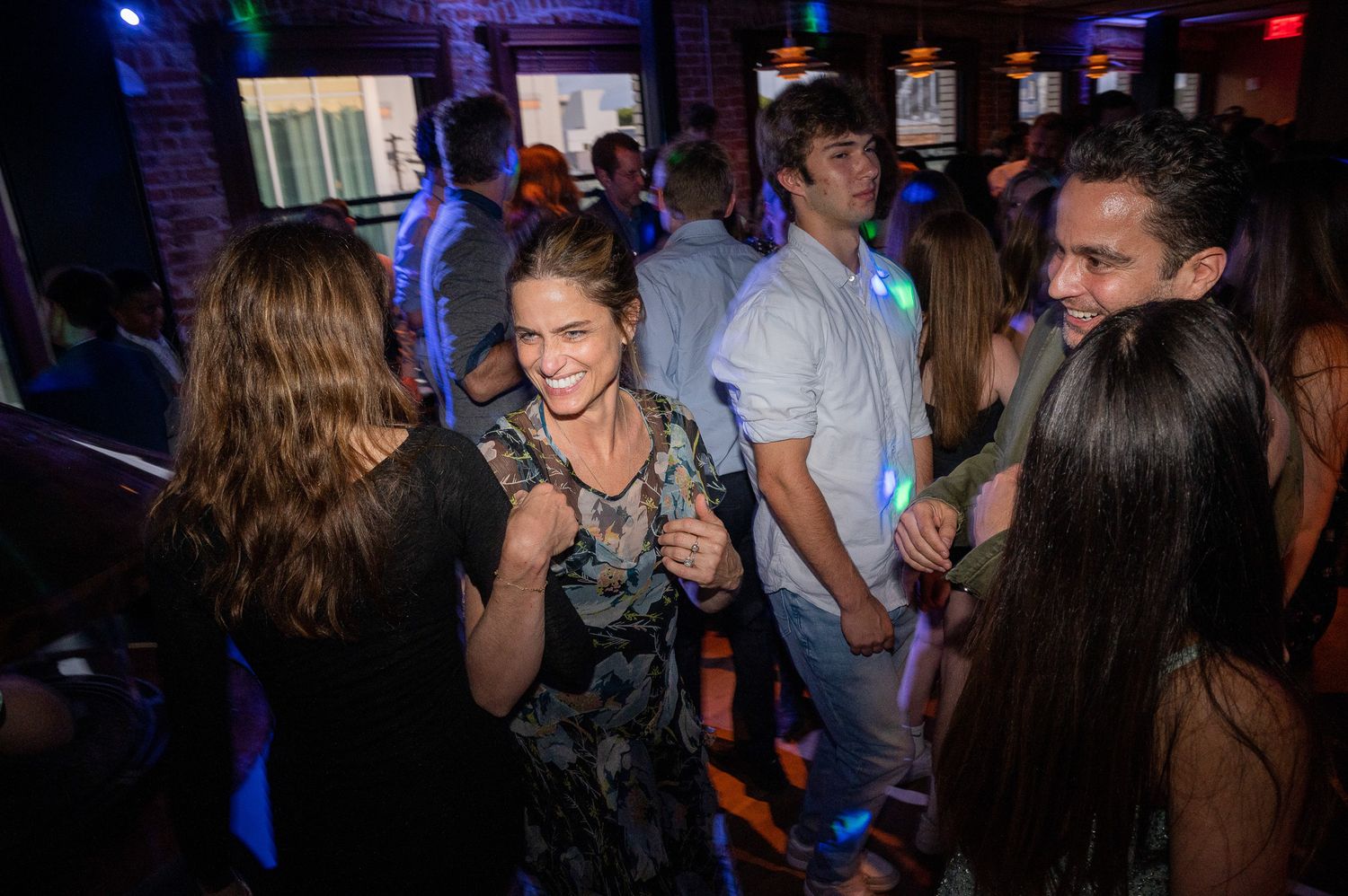 People dancing and socializing at a nightclub with colorful lighting and brick walls.
