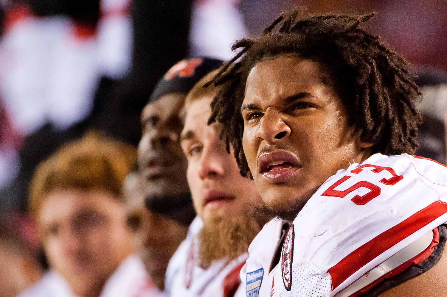Football player in white jersey with red text shown on sidelines with intense expression during game.
