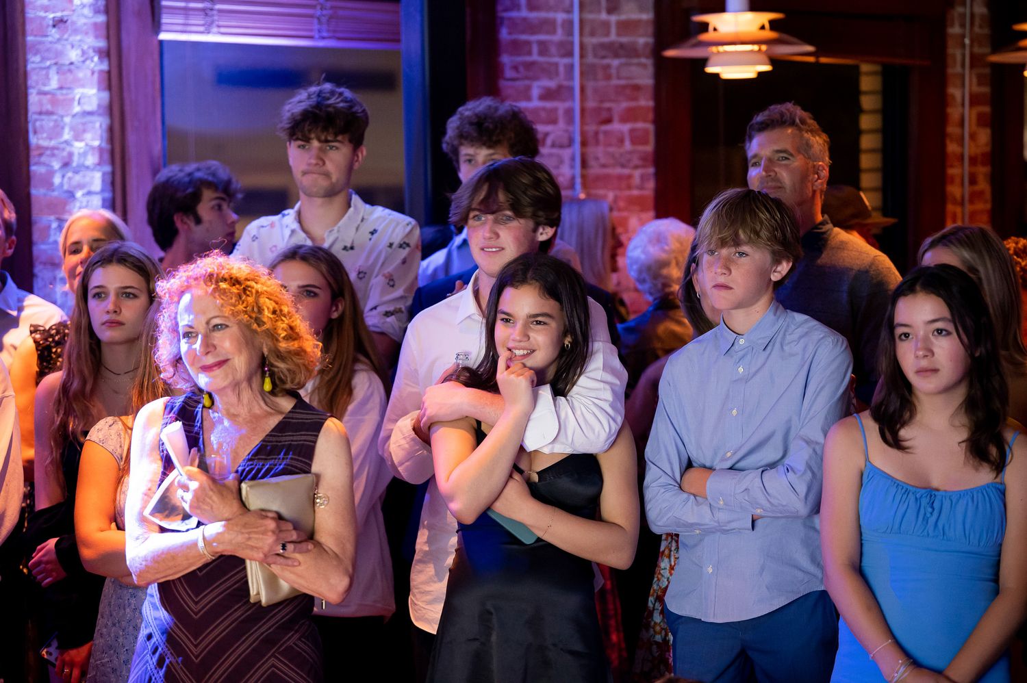 A group of people standing together at an indoor social gathering with brick walls and atmospheric lighting.