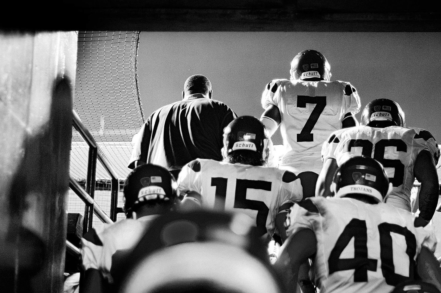 Black and white photo of football players wearing numbered jerseys walking up stadium stairs.