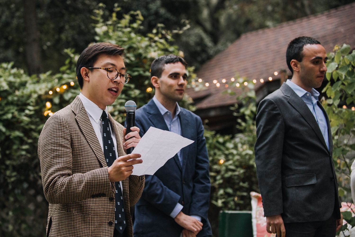 A group of wedding guests engaged in conversation during an outdoor garden reception celebration.