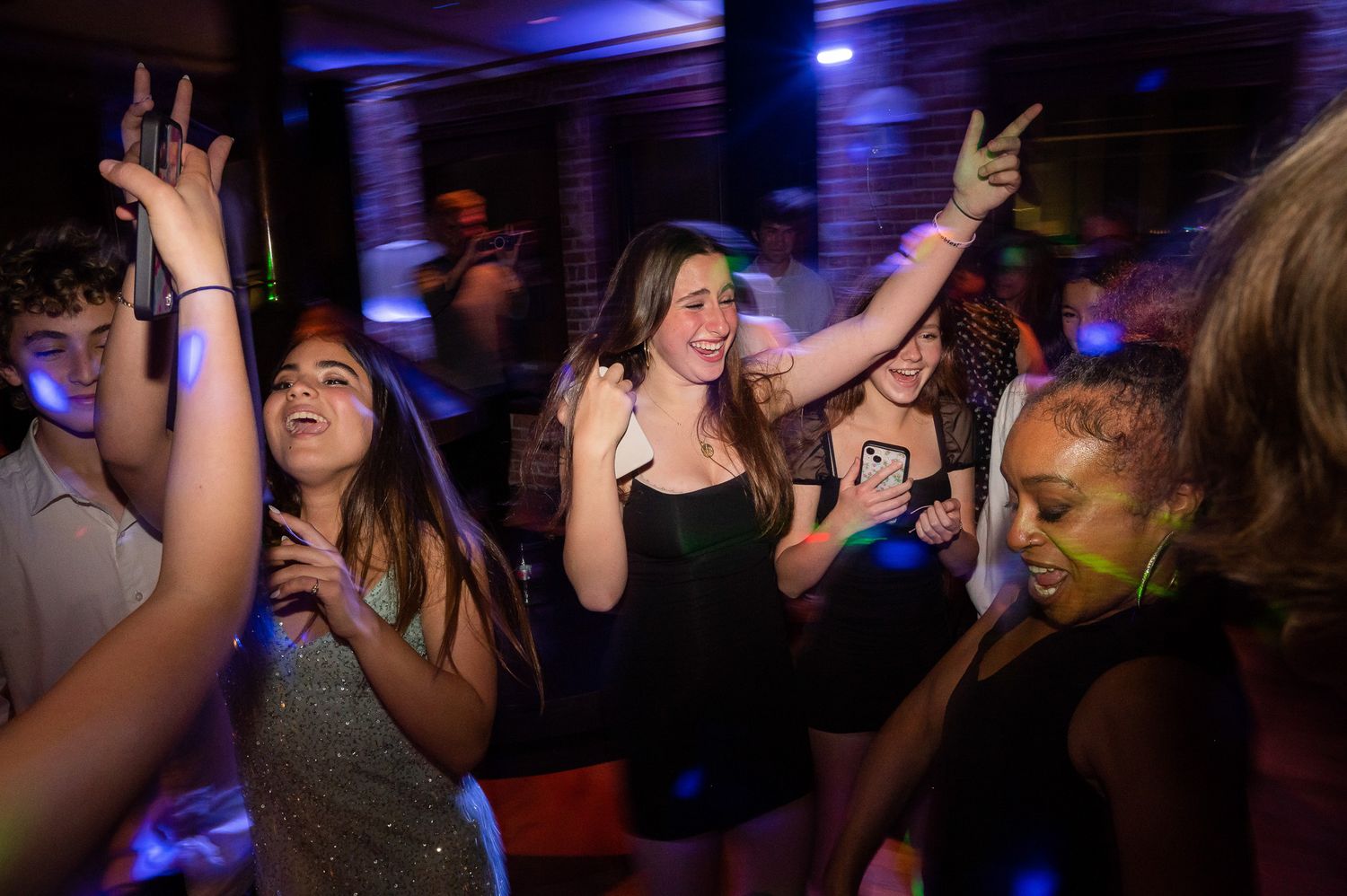 People dancing and raising their hands enthusiastically at a nightclub party with blue lighting.
