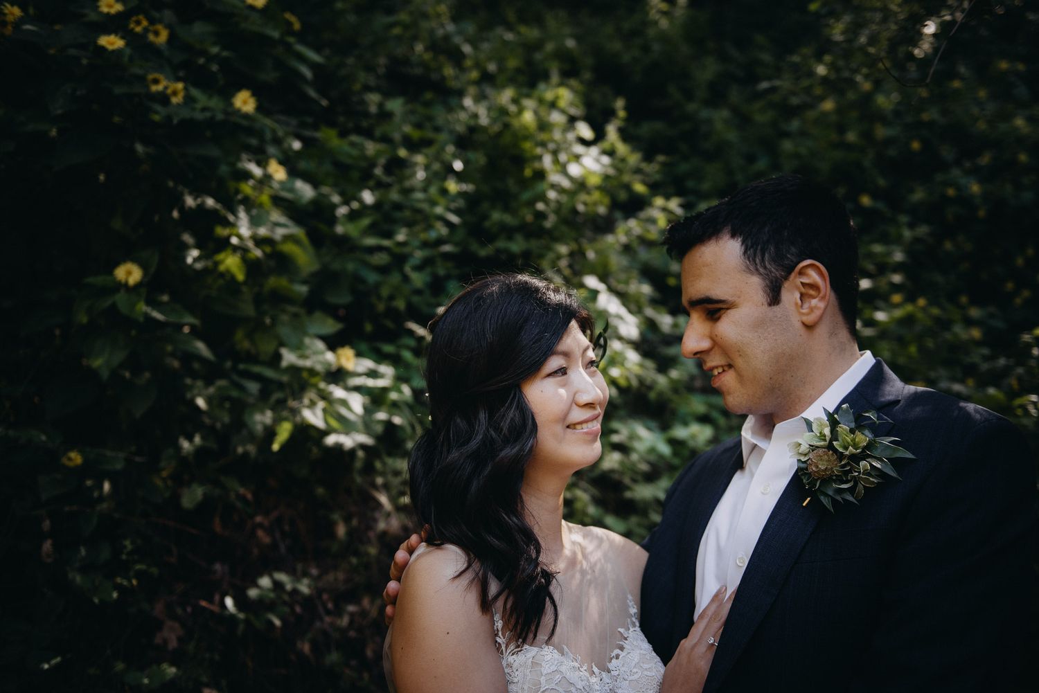 Newlyweds embrace in a romantic forest setting with natural light filtering through the trees.