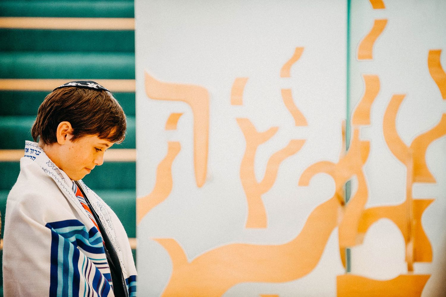 A student stands near a wall with orange abstract artwork painted on it against a teal background.