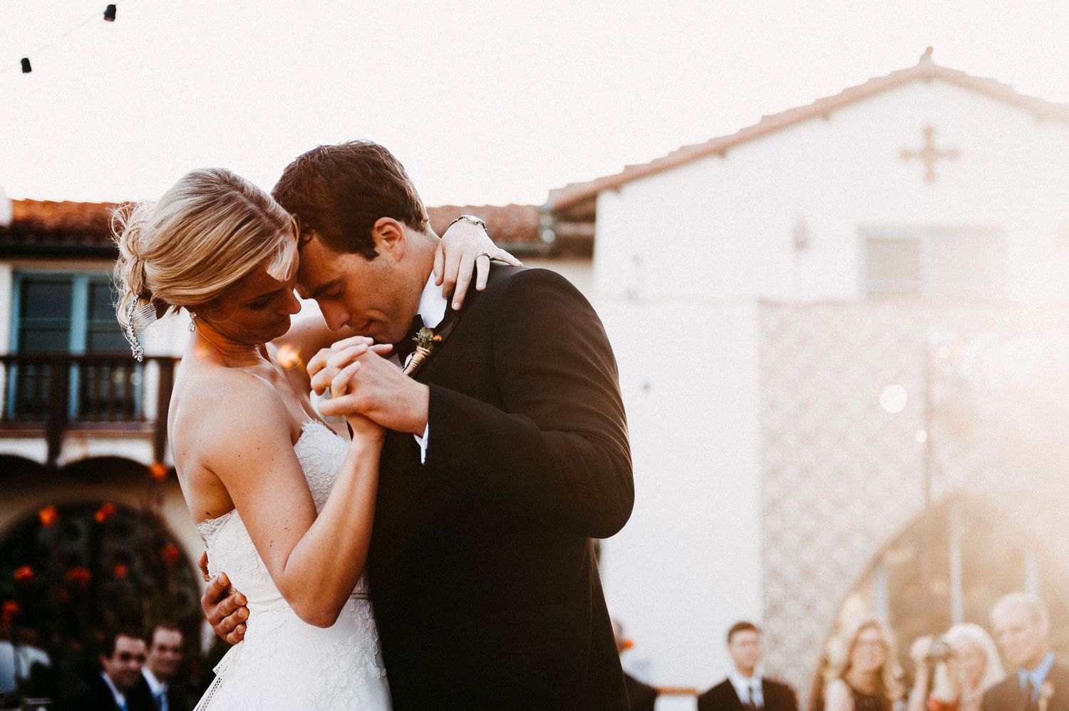 A romantic moment between a couple dancing at sunset outside a white Spanish-style church during their wedding celebration.
